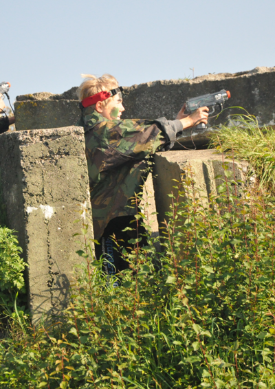Dreng i camouflagetøj med laser pistol gemmer sig bag en mur