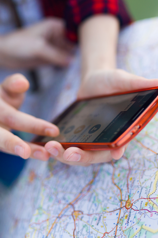 landkort og en der holder mobiltelefon i sine hænder