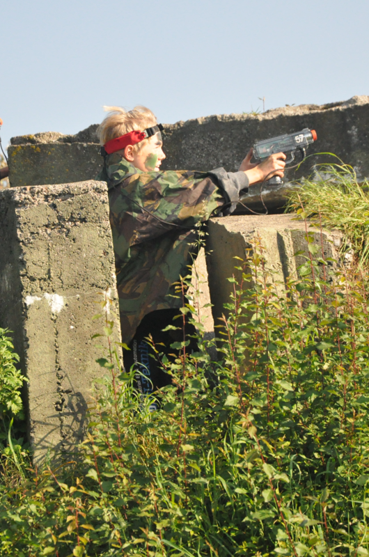 Dreng i camouflagetøj med laser pistol gemmer sig bag en mur